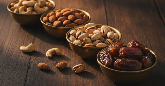 Cashews, almonds, pistachios, and dates in small brass-toned bowls on a dark wooden table